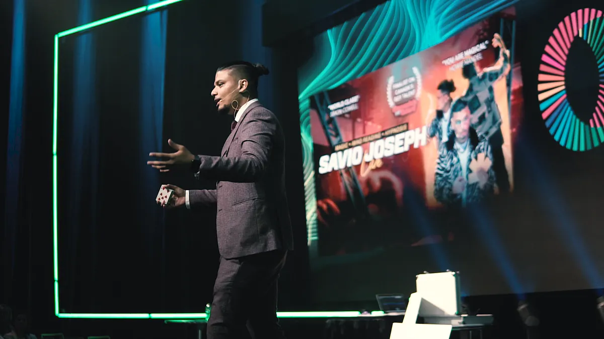 Savio Joseph speaking on a conference stage beside a large screen