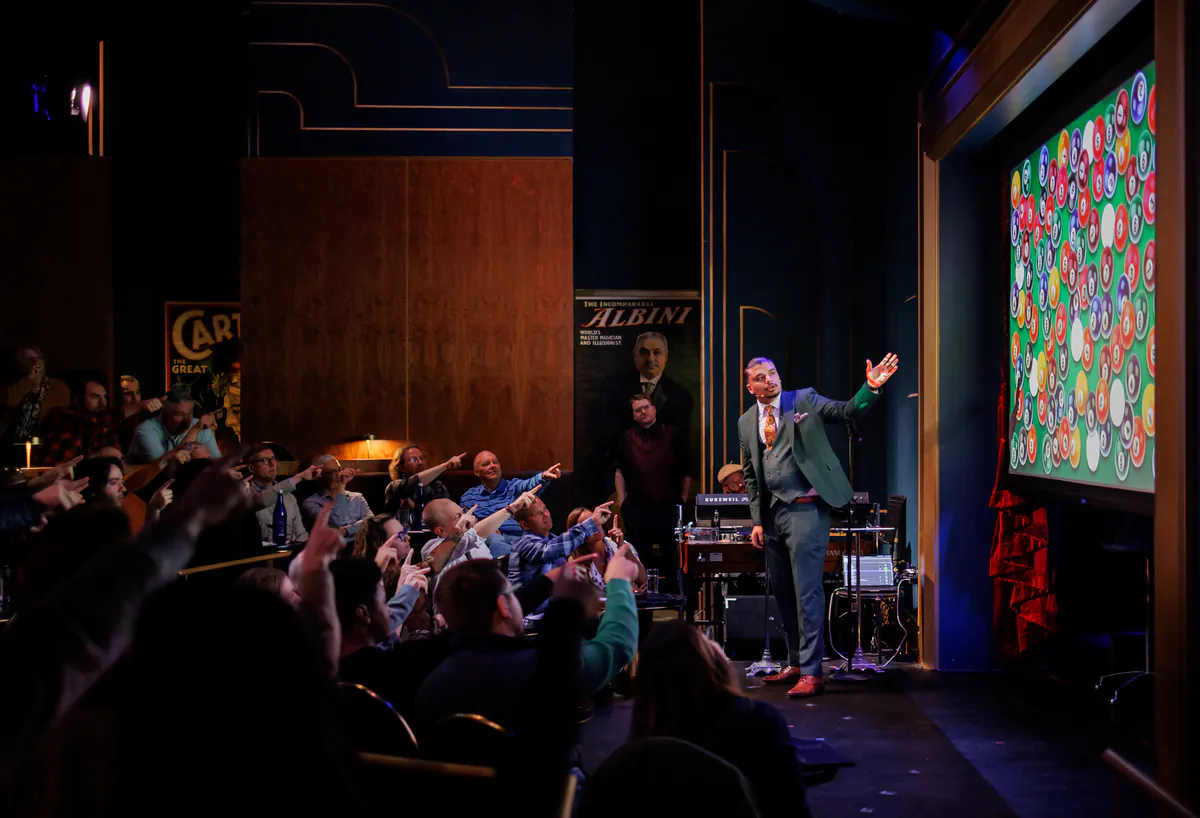 An audience pointing toward Savio Joseph as he gestures from the stage